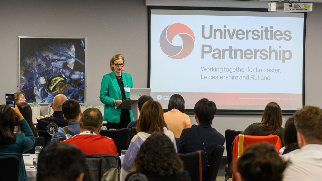 A senior leader from the University of Leicester presents to an audience backed by a Universities Partnership slide back drop